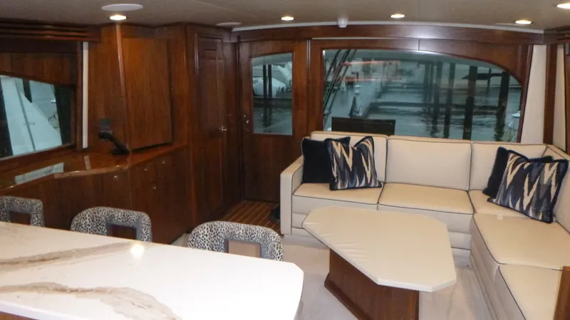Slide: The Image of Salon with Elegant Seating Area This inviting salon on the 2022 Viking 68 Convertible, 'Tax Man,' features a luxurious L-shaped sofa adorned with stylish accent pillows. The warm wood finishes and ample natural light create an elegant and cozy atmosphere. A modern bar area with chic sto - 6862322
