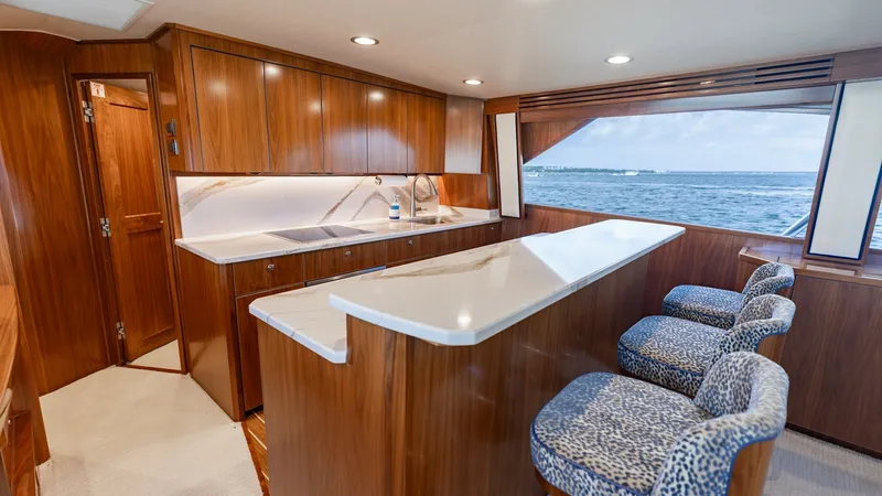 Slide: The Image of Galley with Breakfast Bar Seating This elegant galley on the Viking 68 Convertible features rich wood cabinetry and a sleek, spacious countertop. The breakfast bar provides comfortable seating with stylish patterned stools, perfect for casual dining or entertaining. Large windows offer st - 7463803