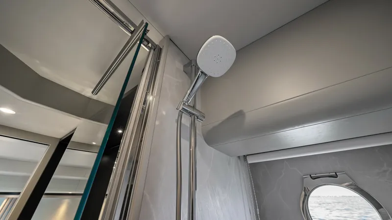 Slide: The Image of Luxury Bathroom Shower with Ocean View This modern bathroom on the Absolute Navetta 58 features a sleek shower with polished chrome fixtures and a handheld showerhead. The elegant marble finish adds a touch of luxury, while the porthole provides a stunning view of the ocean, enhancing the bath - 7018637