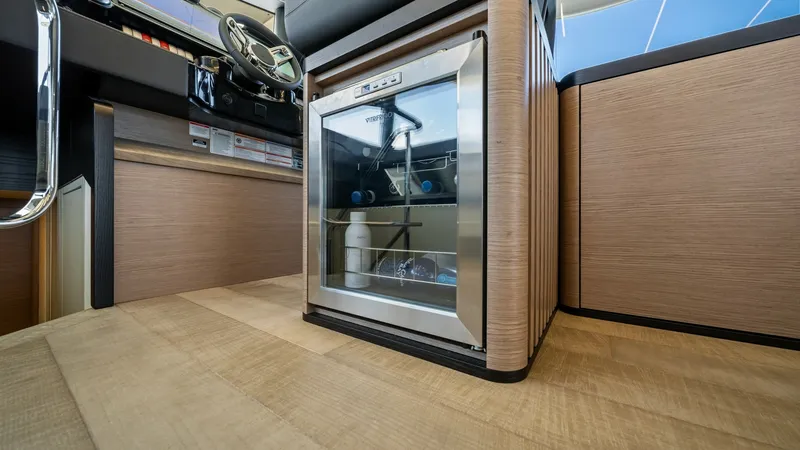 Slide: The Image of Helm Station with Mini Fridge The helm station of the Absolute Navetta 58 features a sleek, integrated mini fridge, adding convenience for long voyages. The contemporary wood finishes and ergonomic layout enhance the functionality and style of the command center. Ample natural light f - 7018643