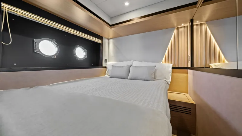 Slide: The Image of Guest Cabin with Portholes The guest cabin of the Absolute Navetta 58 exudes modern elegance with its sleek design and soft ambient lighting. It features a comfortable double bed adorned with plush bedding, surrounded by rich wood finishes and contemporary accents. Twin portholes p - 7018629