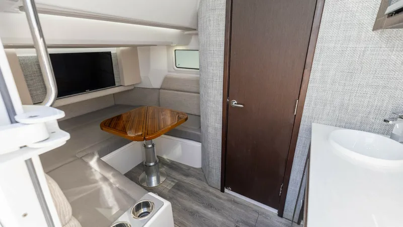 Slide: The Image of Cozy Interior Cabin with Seating Area The interior cabin of the 2023 Everglades 455 Center Console, 'Cash Cow', showcases a comfortable seating area with a polished wooden table, perfect for relaxation or casual dining. The space is complemented by a modern design featuring light-toned uphols - 7095072