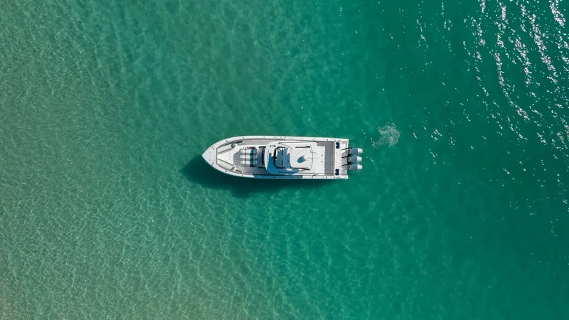 Slide: The Image of Aerial View of Center Console This aerial shot showcases the sleek design of the 2023 Everglades 455 Center Console, 'Cash Cow.' The vessel glides effortlessly over clear turquoise waters, highlighting its streamlined hull and spacious deck layout. Perfect for both leisure and perform - 7095094