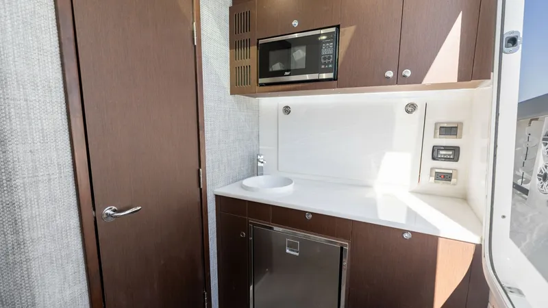 Slide: The Image of Galley with Modern Appliances The galley on the Everglades 455 Center Console offers sleek cabinetry and a compact, efficient design. It features a built-in microwave, a stainless steel refrigerator, and a stylish sink with ample counter space. The wood finishes and modern fixtures cr - 7095076