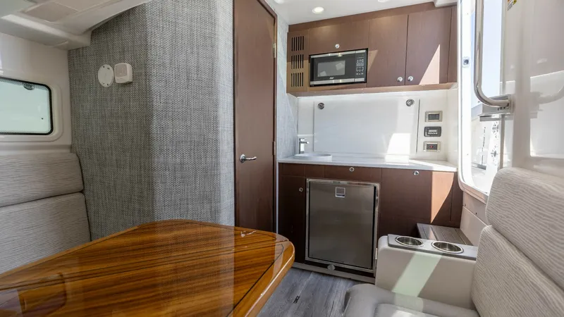 Slide: The Image of Galley and Dinette Area The galley and dinette area of the 2023 Everglades 455 Center Console features a compact yet functional design. It includes a sleek countertop with a built-in microwave and fridge, complemented by rich wood cabinetry. The adjacent dinette offers a polishe - 7095074