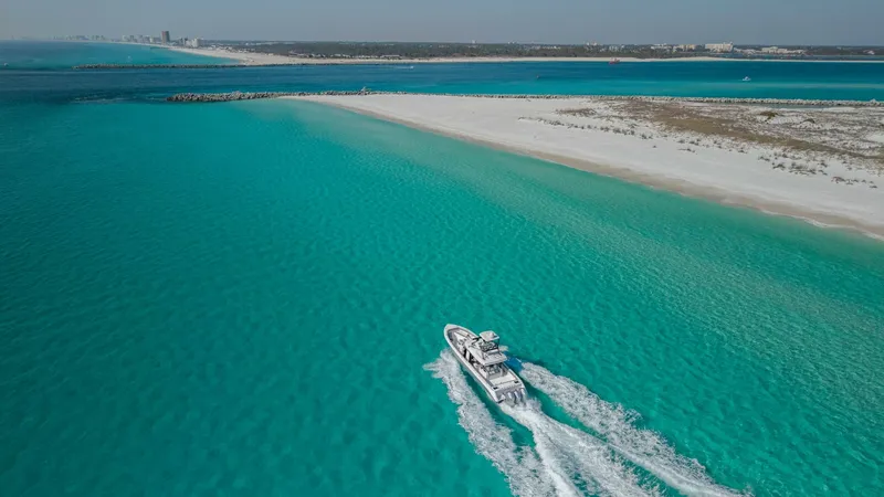 Slide: The Image of Aerial View of Yacht in Open Water The 2023 Everglades 455 Center Console, named 'Cash Cow', glides effortlessly through crystal-clear turquoise waters. Captured from above, this sleek vessel showcases its impressive speed and elegant design against a stunning coastal backdrop. The yacht's - 7095103