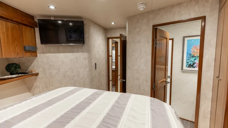 Slide: The Image of Guest Stateroom with Ensuite Access This inviting guest stateroom features a comfortable bed with elegant striped bedding, complemented by warm wood accents. A wall-mounted TV offers entertainment, while the ensuite bathroom ensures privacy and convenience. Soft lighting and tasteful decor - 7150187
