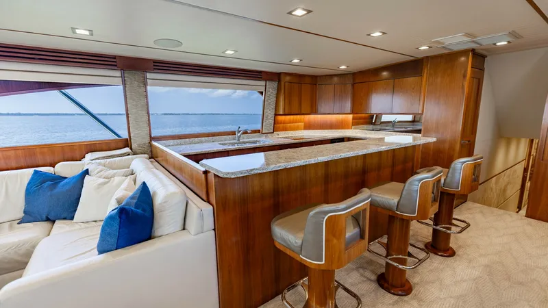 Slide: The Image of Galley and Lounge Area View This image showcases the elegant galley and lounge area of the 2016 Viking 80 Convertible. The space features rich wood cabinetry and a sleek granite countertop bar with comfortable seating for three. Large windows provide natural light and stunning ocean - 7150165