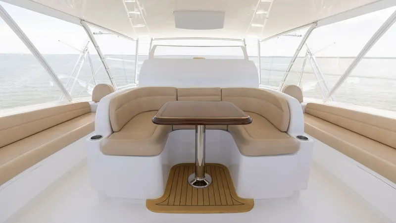 Slide: The Image of Flybridge Seating Area with Table This spacious flybridge on the 2016 Viking 80 Convertible features a comfortable, curved seating arrangement with plush beige cushions, ideal for social gatherings. The central varnished wooden table adds elegance, perfect for dining or entertaining. Surr - 7150207