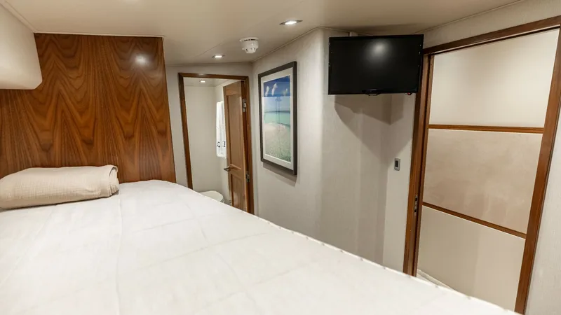 Slide: The Image of Guest Stateroom with Ensuite Access This inviting guest stateroom on the 2016 Viking 80 Convertible offers a cozy retreat with a large bed and luxurious wood finishes. The room features modern amenities including a wall-mounted TV and integrated lighting for a comfortable stay. Convenient e - 7150194