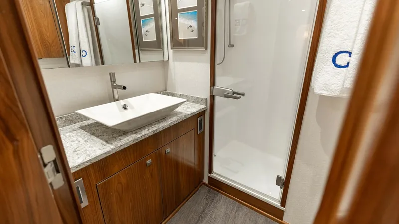 Slide: The Image of Elegant Yacht Bathroom with Shower This luxurious bathroom on the 2016 Viking 80 Convertible features a sleek, modern design with a spacious shower and elegant vessel sink. The warm wood cabinetry and polished granite countertop create a sophisticated ambiance, while the ample mirror and l - 7150178