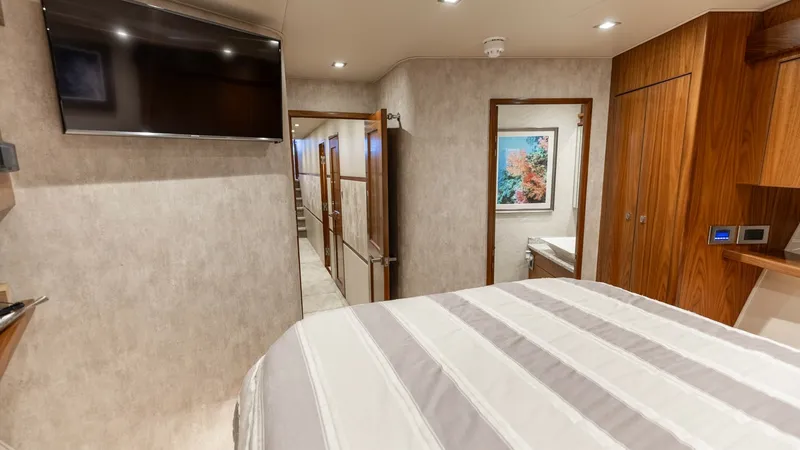 Slide: The Image of Guest Stateroom with Ensuite Access This inviting guest stateroom features a comfortable bed with a stylish striped duvet, complemented by warm wooden cabinetry. A wall-mounted flat-screen TV offers entertainment, while recessed lighting provides a cozy ambiance. The ensuite bathroom is eas - 7150188