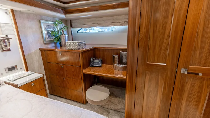 Slide: The Image of Master Stateroom Desk and Storage This luxurious master stateroom on the 2016 Viking 80 Convertible features elegant wood finishes and ample storage options. The built-in desk, complemented by a comfortable stool, provides a practical workspace with natural light from the portside window. - 7150181