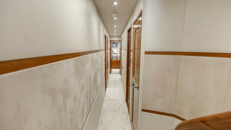 Slide: The Image of Elegant Interior Hallway This image showcases the elegant hallway of the 2016 Viking 80 Convertible, featuring warm wood accents and soft, ambient lighting. The corridor leads to multiple staterooms, offering seamless access throughout the interior. The high-quality finishes and - 7150185
