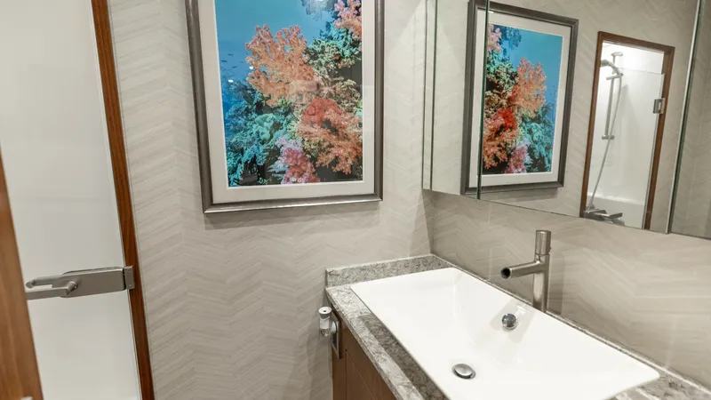 Slide: The Image of Elegant Guest Bathroom Interior This stylish guest bathroom on the 2016 Viking 80 Convertible features a modern sink with a sleek, contemporary faucet set into a polished stone countertop. The room is enhanced by a large mirror and a vibrant coral reef artwork, adding a touch of color a - 7150189