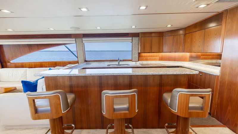 Slide: The Image of Galley with Bar Seating This elegant galley features sleek wooden cabinetry and modern appliances, complemented by a polished granite countertop. Three plush bar stools provide a comfortable seating area, perfect for entertaining while enjoying a panoramic view through expansive - 7150166