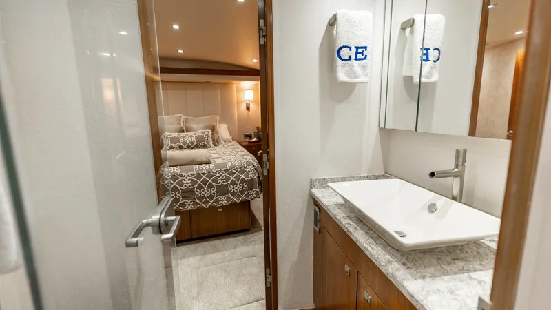 Slide: The Image of Ensuite Bathroom with Stateroom View This elegant ensuite bathroom features a sleek vessel sink atop a marble countertop, complemented by warm wood cabinetry. The sophisticated design includes plush towels and ample mirror space, enhancing the luxurious feel. Beyond, a glimpse into the cozy - 7150177