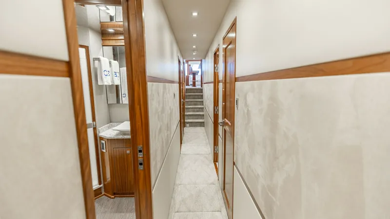 Slide: The Image of Elegant Corridor with Access to Cabins This image showcases the sleek corridor of the 2016 Viking 80 Convertible. The hallway is lined with rich wood accents and soft lighting, creating a welcoming atmosphere. Access to various cabins is provided, with a glimpse into a well-appointed bathroom - 7150173
