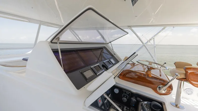 Slide: The Image of Flybridge Helm Station with Controls The image showcases the flybridge helm station of the 2016 Viking 80 Convertible. It features an advanced navigation system with multiple displays set into a sleek console. The polished wood steering wheel and comfortable seating provide a sophisticated a - 7150204