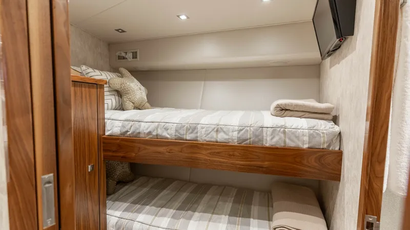 Slide: The Image of Bunk Cabin with TV This cozy bunk cabin on the 2016 Viking 80 Convertible features two neatly arranged bunks with elegant wood finishes. Soft lighting and a wall-mounted TV enhance comfort and convenience, making it an inviting space for relaxation. The warm tones and plush - 7150190