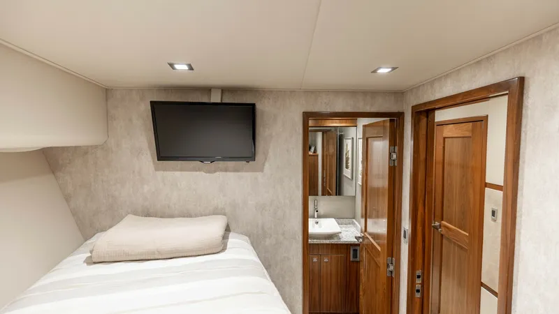 Slide: The Image of Guest Stateroom with Ensuite Access This inviting guest stateroom features a cozy berth with luxurious linens and integrated overhead lighting for a warm ambiance. A wall-mounted flat-screen TV offers entertainment, while the ensuite bathroom provides convenience and privacy. Rich wood fini - 7150191