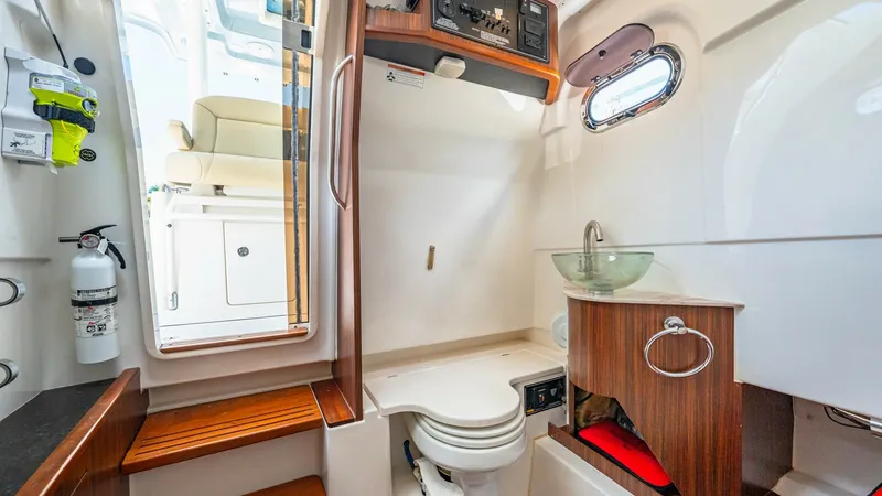 Slide: The Image of Luxurious Onboard Head with Teak Accents The 2019 Pursuit 328 features a well-appointed head with elegant teak accents and a modern glass bowl sink. Natural light filters through a porthole, enhancing the space's bright and airy feel. Efficiently designed, this area provides both comfort and fun - 7095046