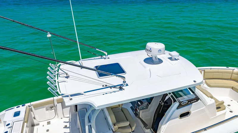 Slide: The Image of Flybridge and Helm Station The 2019 Pursuit 328 features a sleek flybridge with integrated radar and rod holders, perfect for fishing enthusiasts. The helm station offers a comfortable seating arrangement with easy access to controls, surrounded by a 360-degree view of the ocean. I - 7095016