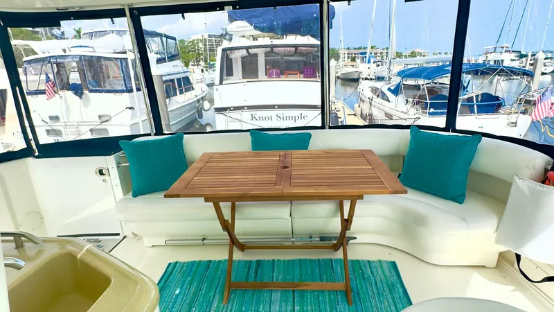 Slide: The Image of Enclosed Aft Deck Seating Area This inviting aft deck features a comfortable curved seating arrangement with plush teal-accented cushions, perfect for entertaining or relaxation. The space includes a stylish wooden table, ideal for alfresco dining, set against a backdrop of large windo - 7150626