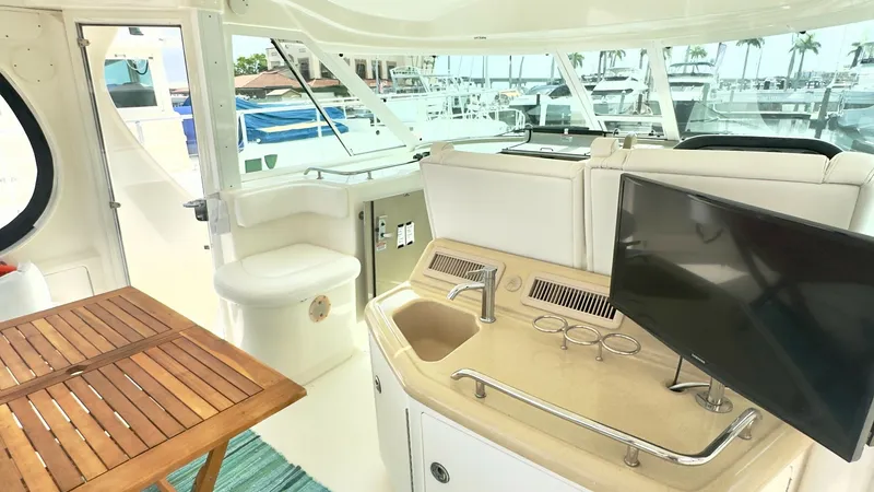 Slide: The Image of Upper Deck Entertainment Area The upper deck of the 2006 Sea Ray 40 Motor Yacht features a stylish entertainment space with a built-in sink and a mounted flat-screen TV, perfect for leisure and socializing. The area includes a wooden table, offering a cozy spot for dining or drinks, e - 7150632