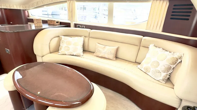 Slide: The Image of Salon Seating Area with Coffee Table The salon of the 2006 Sea Ray 40 Motor Yacht features an elegant curved sofa upholstered in luxurious cream leather, complemented by decorative cushions. A polished wood coffee table serves as the centerpiece, offering functionality and style. Large windo - 7150639