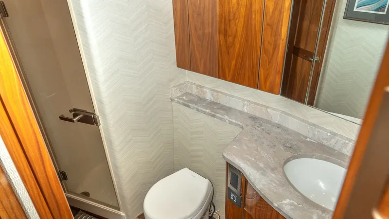 Slide: The Image of Elegant Yacht Ensuite Bathroom This well-appointed ensuite bathroom on the 2017 Viking 55 Convertible features a sleek marble countertop and integrated sink, offering a touch of luxury. The rich wood cabinetry provides ample storage, while the glass-enclosed shower adds a modern touch. - 7180040