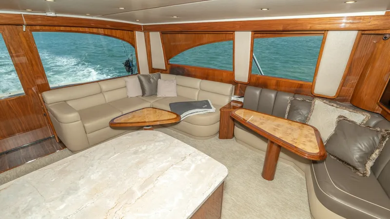 Slide: The Image of Spacious Salon with Panoramic Views The salon of the 2017 Viking 55 Convertible, Marilee, offers a luxurious and comfortable space with plush L-shaped seating and elegant wood finishes. Large windows provide panoramic views, enhancing the open feel and inviting natural light. The polished w - 7180027