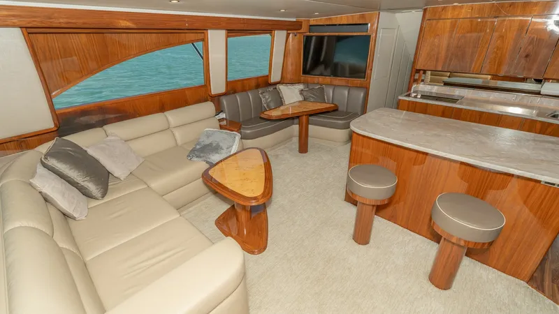 Slide: The Image of Spacious Salon with Galley The salon of the 2017 Viking 55 Convertible offers a luxurious and inviting space with plush, cream-colored seating and a stylish wooden coffee table. Large windows provide stunning ocean views, enhancing the natural light and ambiance. The adjacent galle - 7180024
