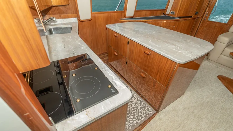 Slide: The Image of Galley with Modern Appliances This well-appointed galley on the Viking 55 Convertible features sleek marble countertops and modern induction cooktop, offering both style and functionality. The rich wood cabinetry complements the elegant design, providing ample storage space. Large win - 7180034