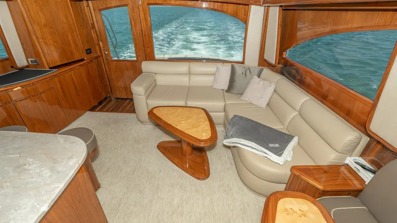 Slide: The Image of Spacious Salon with Ocean Views The salon of the 2017 Viking 55 Convertible boasts a luxurious L-shaped leather sofa, complemented by rich wood finishes and elegant accents. Large windows offer stunning ocean views, enhancing the open and airy ambiance of the space. A sleek, polished co - 7180029