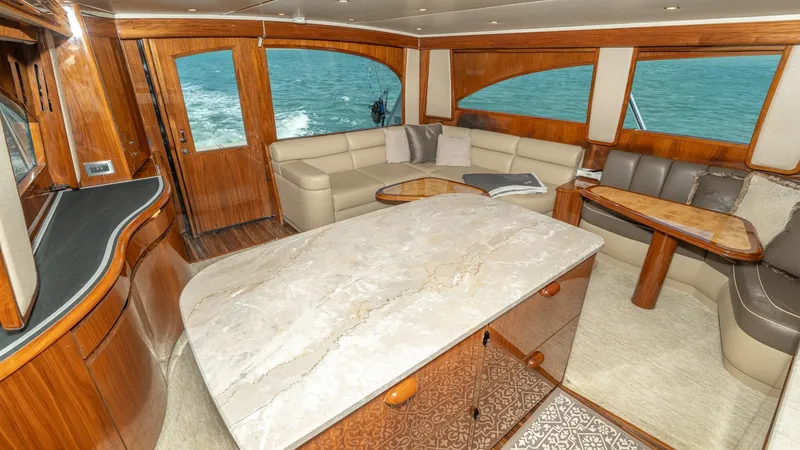 Slide: The Image of Spacious Interior Salon with Seating The salon of the 2017 Viking 55 Convertible offers an inviting space with plush cream-colored seating and elegant wooden finishes. Large panoramic windows provide stunning ocean views, complementing the warm, natural light that fills the room. The central - 7180025