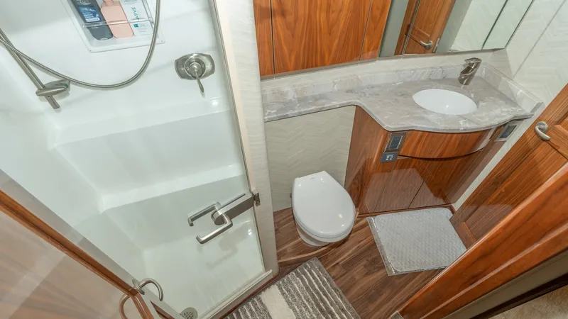 Slide: The Image of Luxurious Ensuite Bathroom This elegant ensuite bathroom on the 2017 Viking 55 Convertible features a sleek glass-enclosed shower and a modern vanity with a polished marble countertop. The warm wood cabinetry adds a touch of sophistication, while the contemporary fixtures provide b - 7180041
