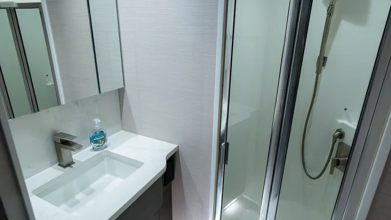 Slide: The Image of Modern Yacht Bathroom with Shower This sleek bathroom on the 2024 Viking 64 Convertible, 'Fish Tank,' features a contemporary design with high-quality finishes. The space includes a stylish vanity with a marble countertop and a modern faucet. Adjacent is a glass-enclosed shower, offering - 7162564