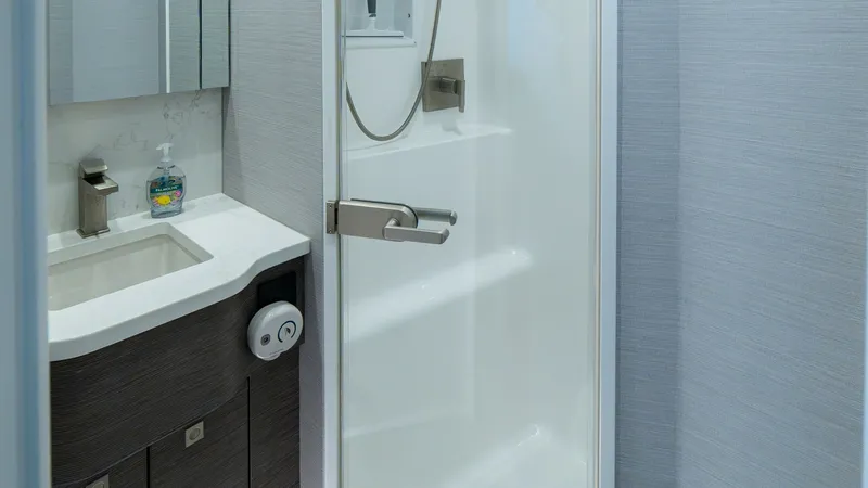 Slide: The Image of Elegant Ensuite Bathroom with Shower This stylish ensuite bathroom aboard the 2024 Viking 64 Convertible features a sleek glass-enclosed shower with modern fixtures. The vanity showcases a contemporary design with a dark wood finish, complemented by polished hardware and ample storage. Brigh - 7162573