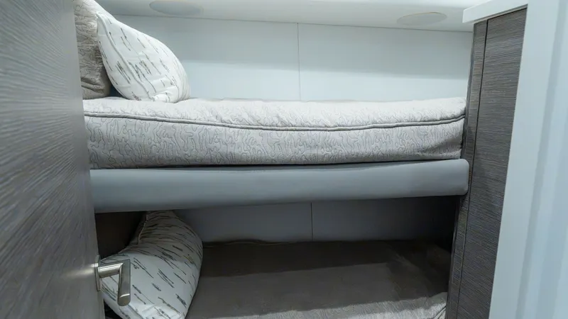 Slide: The Image of Guest Stateroom with Twin Bunks The guest stateroom features cozy twin bunks, offering comfortable accommodations for additional guests. The neutral bedding complements the sleek, modern cabinetry, while built-in lighting provides a warm ambiance. This efficient use of space ensures a r - 7162560