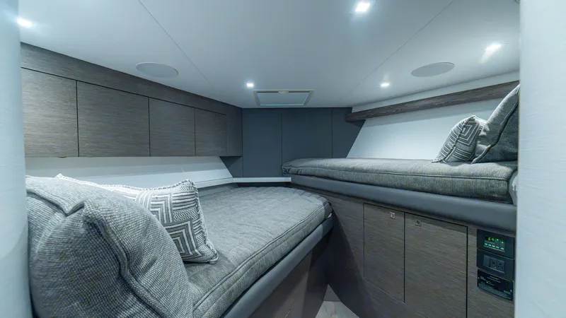 Slide: The Image of Guest Stateroom with Twin Berths This inviting guest stateroom on the 2024 Viking 64 Convertible features twin berths with plush cushions and stylish geometric pillows. The warm wood cabinetry provides ample storage, complemented by sleek overhead lighting. The neutral tones and contempo - 7162561
