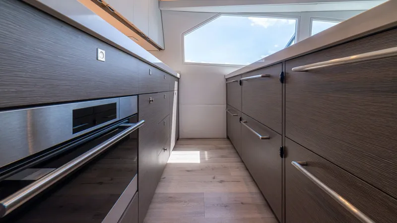 Slide: The Image of Modern Galley with Sleek Finishes This spacious galley on the 2024 Viking 64 Convertible showcases contemporary design with high-end finishes. Dark wood cabinetry complements the stainless steel appliances, creating a sophisticated and functional cooking space. Ample natural light floods - 7162551