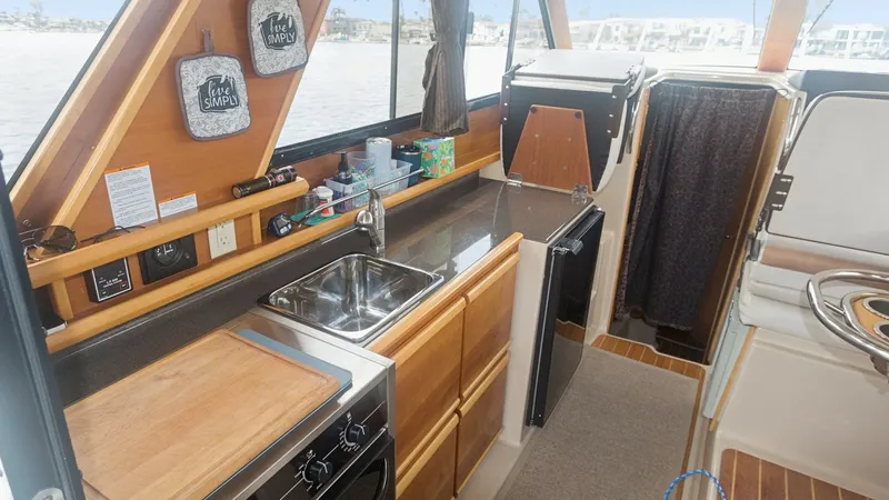 Slide: The Image of Compact Galley with Practical Amenities This well-equipped galley on the 2014 Cutwater 28 Downeast features a sleek countertop with a stainless steel sink and a convenient cutting board. The space includes a compact oven and ample cabinetry for storage, all set against large windows that provid - 7180676