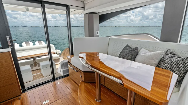 Slide: The Image of Salon with Aft Deck View This image showcases the elegant salon of the 2025 Tiara Yachts 48LE, featuring a sleek, polished wood table and plush seating adorned with decorative pillows. The expansive glass sliding doors open to the aft deck, offering a seamless transition between - 7403640