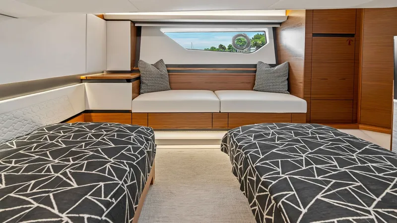 Slide: The Image of Twin Guest Stateroom with Seating This elegant twin guest stateroom features two comfortable single beds adorned with modern geometric patterned bedding. A cozy seating area with plush cushions is positioned beneath a large window, offering natural light and scenic views. The stylish wood - 7403651