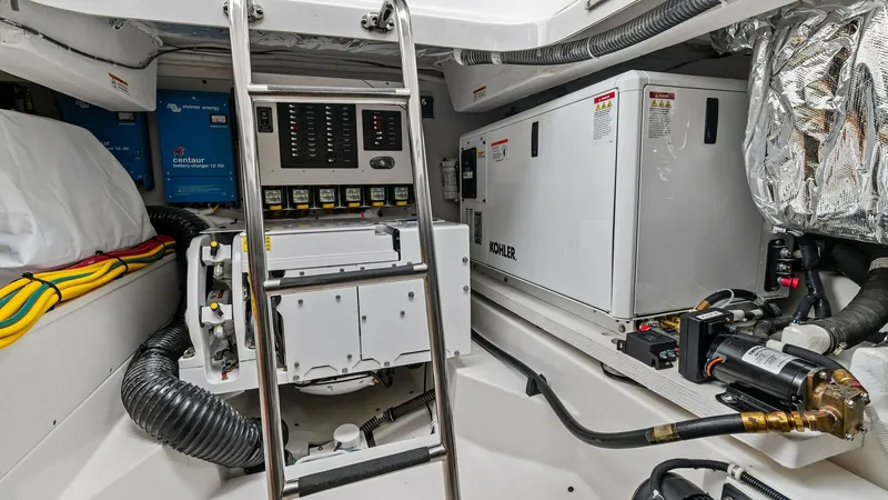 Slide: The Image of Engine Room with Generator and Ladder This image showcases the meticulously organized engine room of the 2025 Tiara Yachts 48LE. The space features a Kohler generator and well-labeled electrical control panels, ensuring efficient power management. The stainless-steel ladder provides easy acce - 7403661