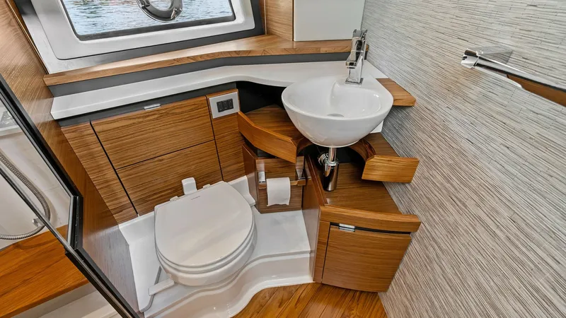 Slide: The Image of Modern Yacht Bathroom with Wood Accents This elegant bathroom on the 2025 Tiara Yachts 48LE features sleek wood cabinetry paired with a contemporary vessel sink, adding a touch of luxury to the space. The curved design of the cabinetry maximizes storage and accessibility, while the large portho - 7403655