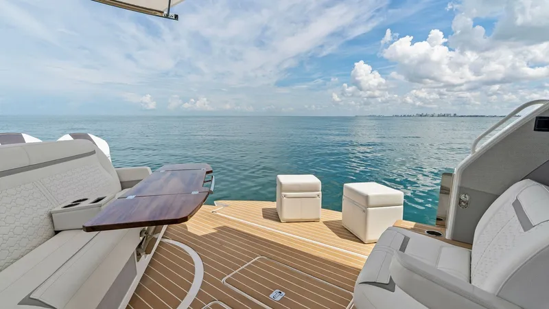 Slide: The Image of Spacious Aft Deck with Seating The aft deck of the 2025 Tiara Yachts 48LE offers a luxurious outdoor living space with plush seating and a sleek wooden table, perfect for alfresco dining. The elegant teak decking complements the serene ocean backdrop, creating a seamless blend of comfo - 7403603