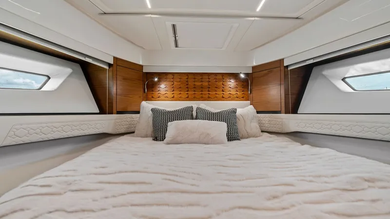 Slide: The Image of Luxurious Forward Stateroom This elegant forward stateroom on the 2025 Tiara Yachts 48LE offers a blend of comfort and style. The plush bedding is complemented by rich wood accents and ambient lighting, creating a warm and inviting atmosphere. Large windows provide ample natural lig - 7403643