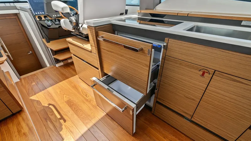 Slide: The Image of Galley with Ample Storage Space The galley of the 2025 Tiara Yachts 48LE showcases a sleek design with high-quality wood cabinetry and ample storage. Featuring modern appliances, including a built-in refrigerator drawer, it offers functionality and style. Natural light floods the area, - 7403629